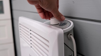 Hand regulating, setting temperature on electric convector, heater thermostate in the room in winter, climate control and energy saving concept