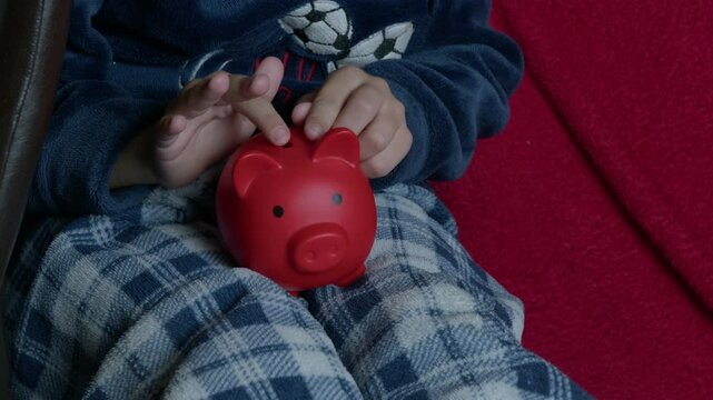 Cute child in pajamas kissing his little red piggy bank. High quality 4k footage