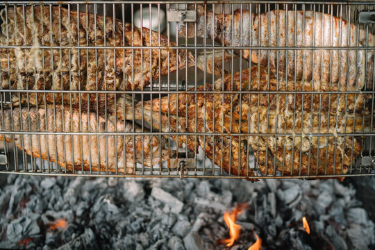 Close-up of multiple fish grilling over hot charcoal fire.