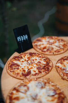 Four delicious pizzas on a round wooden table with sign.