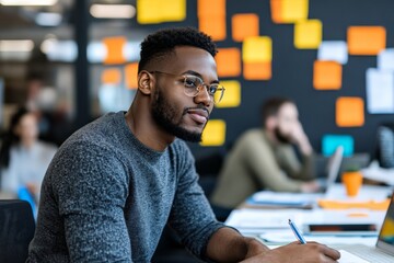 Obraz premium A man with glasses concentrates on his work in a modern, vibrant office setting, surrounded by colorful notes on the wall, capturing a moment of inspiration.