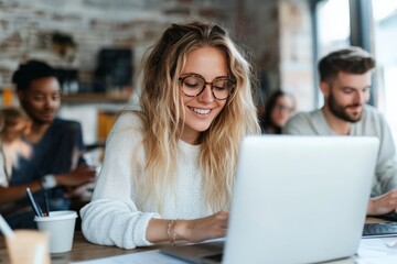Blonde woman in a cozy cafe, wearing glasses, smiles as she types on her laptop, sipping coffee in a warm, relaxed environment with friends in the background.