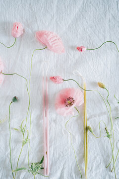 Close-up of pink poppy flowers and pastel candles on fabric.