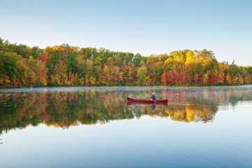 Senior fisherman paddling a red wooden canoe on a beautiful northern Minnesota lake with a small island at dawn during autumn