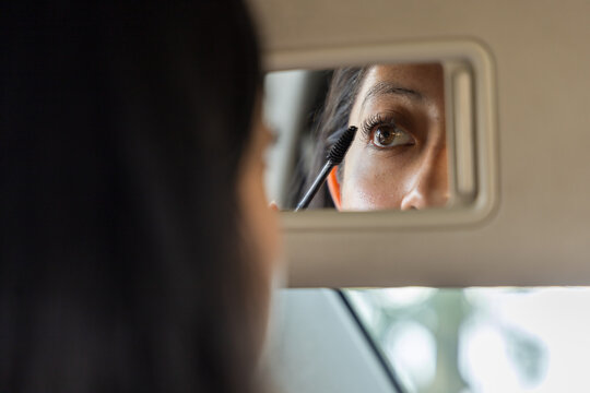 Car visor mirror reflecting a lady painting her eyelashes with mascara