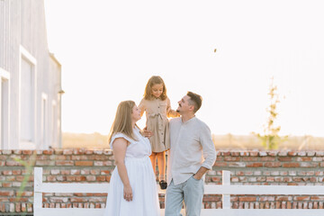 Family shares moment with girl standing on fence edge.