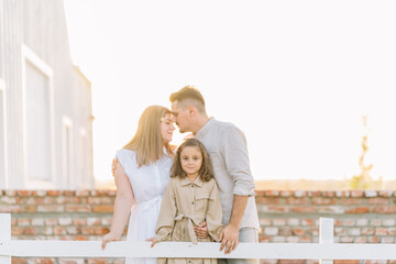 Family shares a moment by a white fence at sunset.