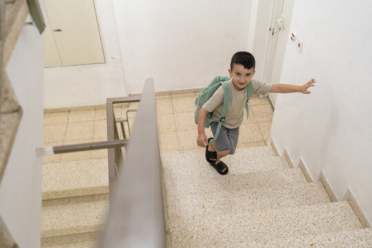 Young boy climbing stairs with backpack in a bright hallway
