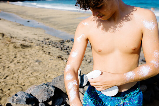 A mid-range shot of a teenage tourist applying sunscreen to his body