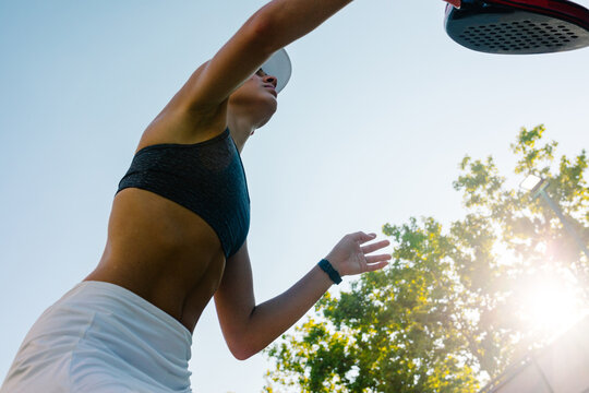 Padel player hitting a ball in a match, seen from below on a sunny day