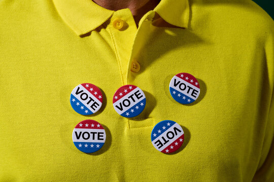 man wearing some vote badges on his polo shirt