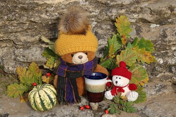 Two teddy bears with a hat and scarf in an environment with autumn decorations and a cup of tea to warm up