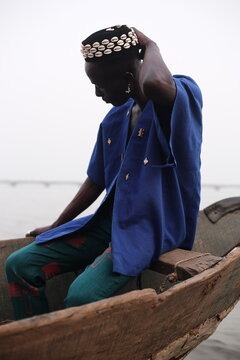  model wearing a hat filled with cowries shells sitting in a boat
