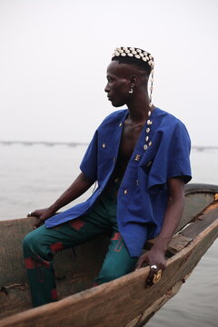 model wearing a hat filled with cowries shells sitting in a boat
