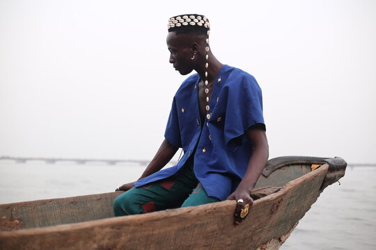  model wearing a hat filled with cowries shells sitting in a boat