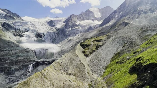 Spectacular drone view of Moiry Glacier in Switzerland, surrounded by rugged alpine terrain and vibrant green slopes. The icy formations and towering peaks capture the pristine beauty of Swiss Alps