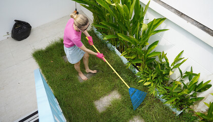 A woman raking the lawn at the backyard of her house 
