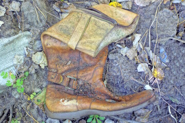 one brown long old leather women boot lies on the gray sand on a summer street