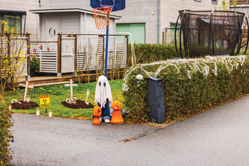 Halloween ghost decoration with pumpkins, fake graves, cobwebs, and zombie warning sign in front yard display. Sweden.