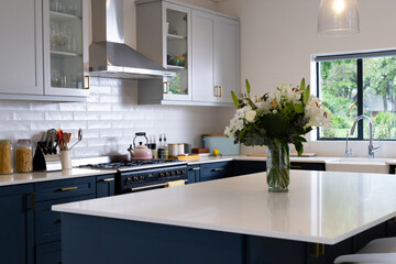 Modern kitchen with elegant white countertops and fresh flowers in vase, at home