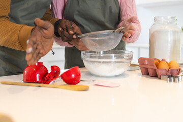 multiracial couple baking together in kitchen, sifting flour into glass bowl, at home