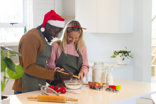 Christmas time, multiracial couple baking, wearing festive holiday attire, at home