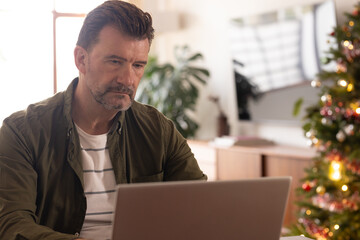 senior man working on laptop at home near decorated Christmas tree