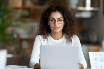 Fototapeta premium A woman wearing glasses is attentively working on her laptop at home, suggesting productivity, concentration, and a modern work environment setting.