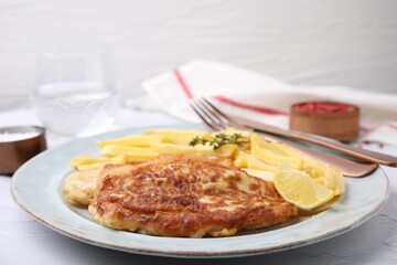 Tasty soda water battered fish, potato chips and lemon slice served on white textured table