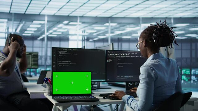 Diverse team of developers in server hub using green screen laptop, looking for misconfigurations. African american IT experts mending data center bugs with chroma key notebook, camera B