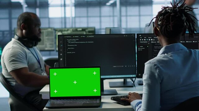 Diverse team of developers in server hub using green screen laptop, looking for misconfigurations. African american IT experts mending data center bugs with chroma key notebook, camera A