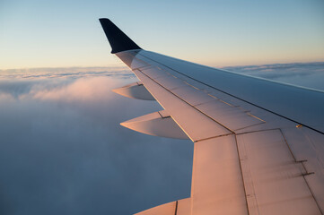 View from airplane window of wing over clouds during flight journey.