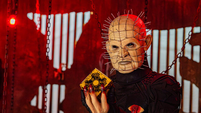 9th Comic Con Convention In GUAYAQUIL, ECUADOR - AUG 04, 2024 - Realistic Pinhead character cosplay holding puzzle box in horror-themed setting with dramatic red lighting.