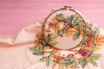 An embroidery hoop with a bright floral pattern is shot close-up against a pale pink background. Do-it-yourself aesthetic installation.