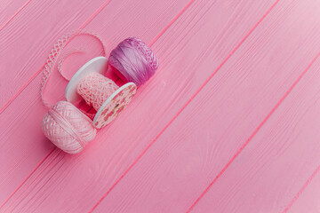 Colorful yarn and sewing tools lie neatly on a bright pink wooden surface, creating a fun craft...