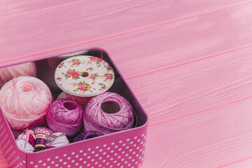 Craft supplies in a polka-dot tin box with pink and purple yarn, ribbon, and sewing accessories on...