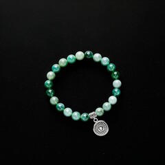 Jade beaded stretch bracelet with silver charm on plain black dark background