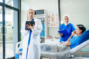 Two Muslim female doctors check the medical history and symptoms of a male patient lying in bed after surgery at the hospital, monitoring his recovery and health status