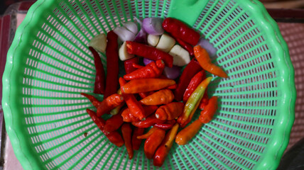 A vibrant assortment of fresh red and orange chili peppers, garlic cloves, and shallots in a green...