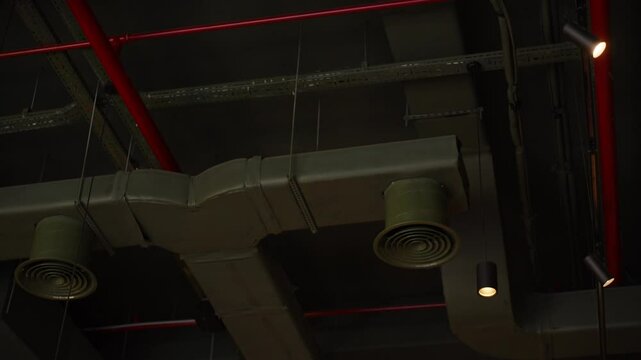 Close-up view of ductwork and pipes in an industrial-style ceiling, featuring cylindrical vents and spotlights, emphasizing urban design and functionality.
