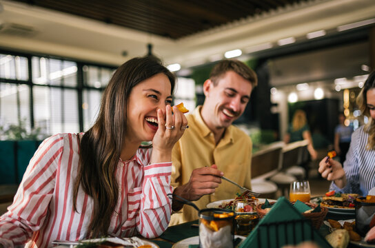 Group of happy friends eating lunch together in a restaurant. They eat delicious salads and hamburgers.
