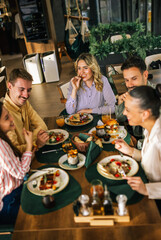 Group of happy friends eating lunch together in a restaurant. They eat delicious salads and...