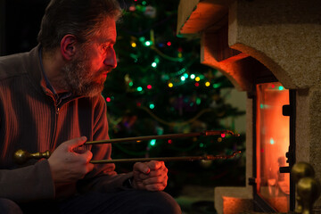 Man sits in front of burning fireplace. Behind Christmas tree