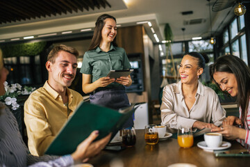 Group of people ordering food from the waitress. Waitress writing orders down on tablet. Undecided people reading the menu while the waitress waits and helps them.