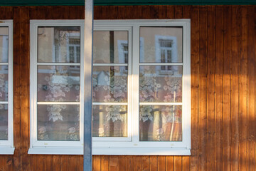 A window with a floral patterned curtain is reflected in the window of a buildin