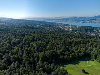 Fototapeta premium Aerial view of Swiss City of Zürich with Lake Zürich and cityscape and golf course in the foreground on a sunny summer morning. Photo taken July 6th, 2024, Zurich, Switzerland.