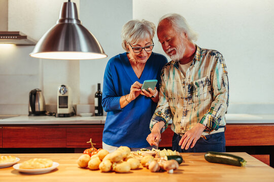 Senior couple reading recipe together while standing in kitchen. - Powered by Adobe