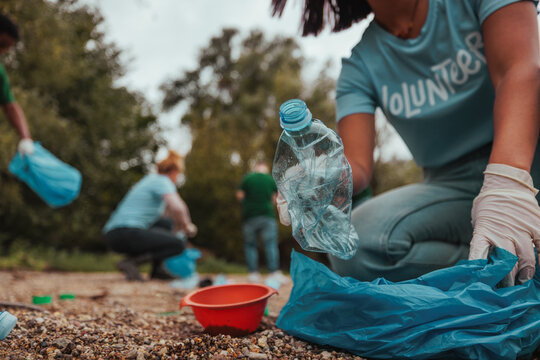Volunteer picking up plastic bottle in polluted park during cleanup event
