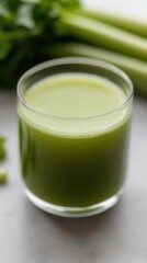 Refreshing green celery juice in a glass with fresh crunchy celery stalks on a light background