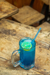 Blue mojito with lemon piece, blue mojito placed in a wooden dining table with blue color straw